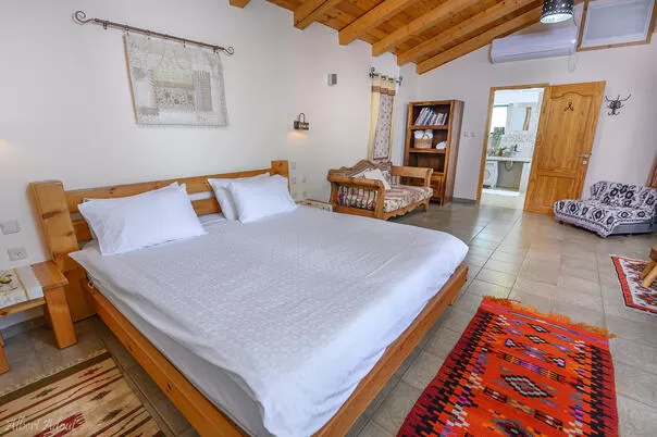 In the center of the large bedroom of the Pearl is a wooden king size bed offered with bright linens - Idyllia| Hapnina Beit Even Yukrateim, Upper Galilee