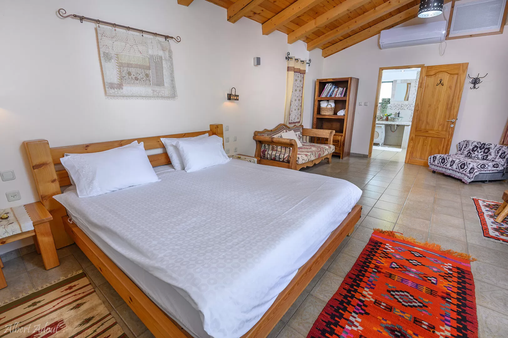 In the center of the large bedroom of the Pearl is a wooden king size bed offered with bright linens - Idyllia| Hapnina Beit Even Yukrateim, Upper Galilee