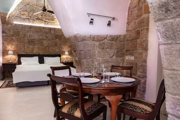 חדר שינה חמים עם קירות אבן, מיטה, שולחן עגול מעץ וכיסאות, ומאוורר תקרה - עלמא- סוויטות בוטיק מעוצבות, סוויטה בצפון, עכו, גליל מערבי
