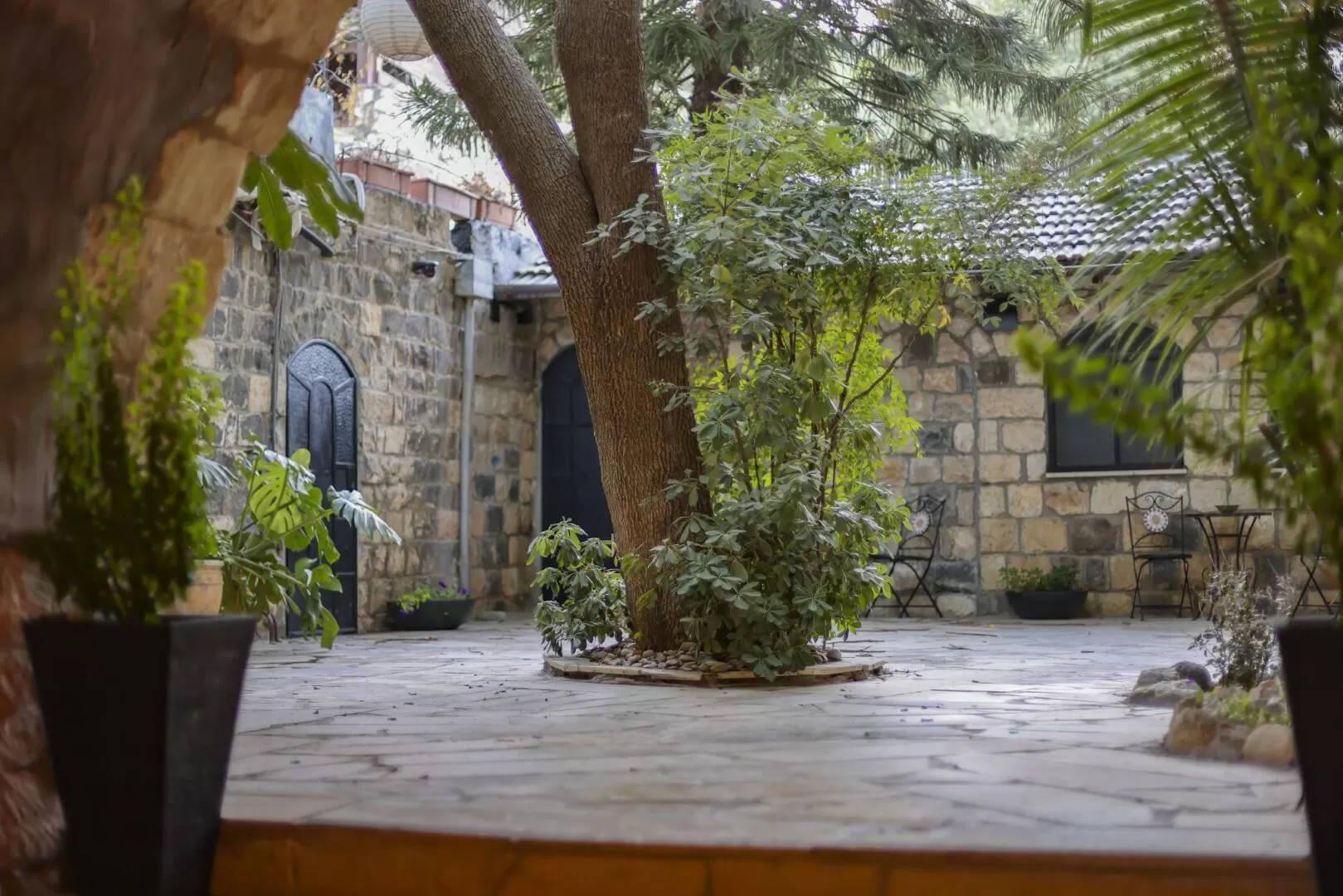 חצר אבן בראש פינה עם עץ מרכזי, קירות אבן ודלתות שחורות - פינה בראש, מלון בוטיק בצפון, ראש פינה, גליל עליון